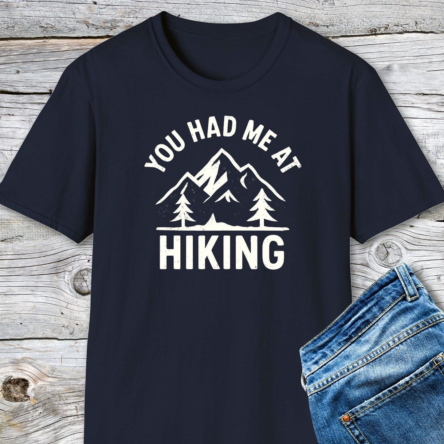 You Had Me At Hiking T-Shirt with mountain graphic, showcasing comfort and durability, ideal for outdoor enthusiasts. Paired with blue jeans on a wooden background.