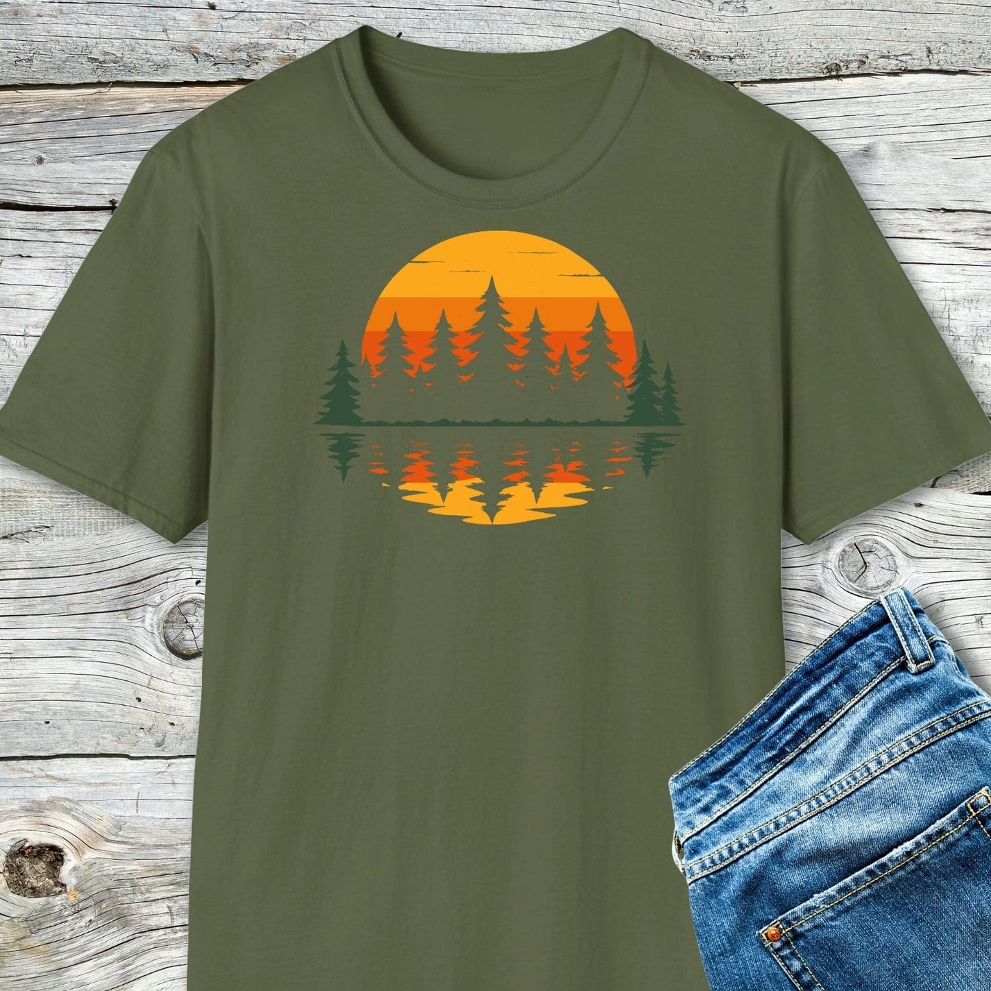 Retro Sunset Pines T-Shirt with evergreen trees and sunset graphic, laid flat next to blue jeans, highlighting its adventure-ready design and durable, eco-friendly print.