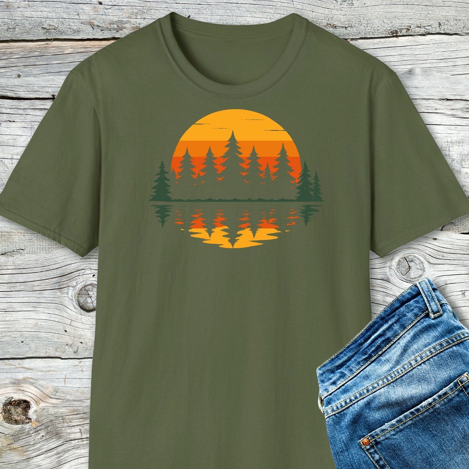 Retro Sunset Pines T-Shirt with evergreen trees and sunset graphic, laid flat next to blue jeans, highlighting its adventure-ready design and durable, eco-friendly print.