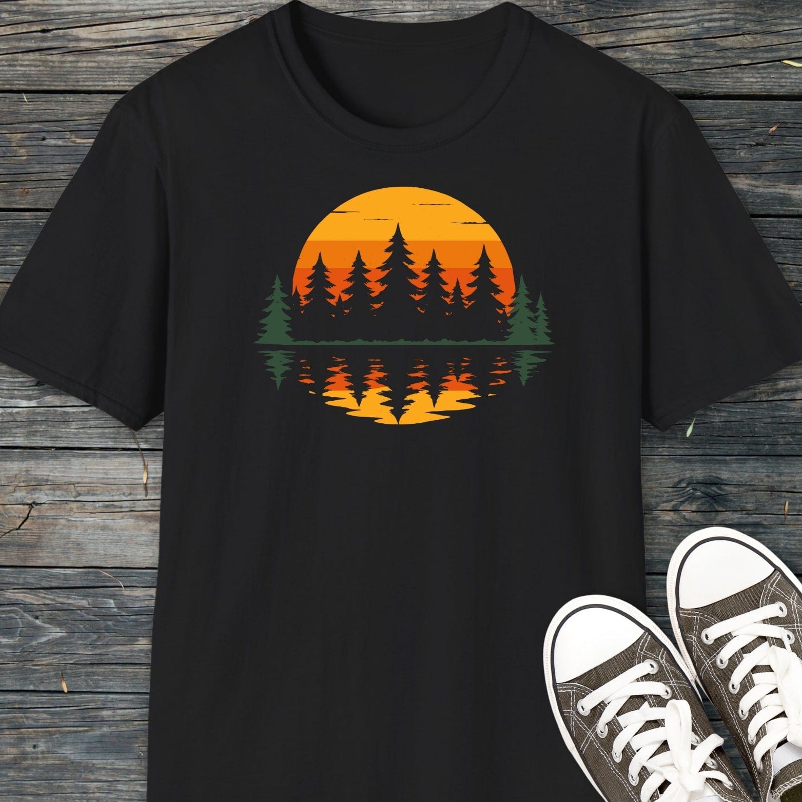 Retro Sunset Pines T-Shirt on wooden surface, showcasing a vibrant sunset and evergreen tree design, emphasizing comfort and durability with pre-shrunk ring-spun cotton fabric.