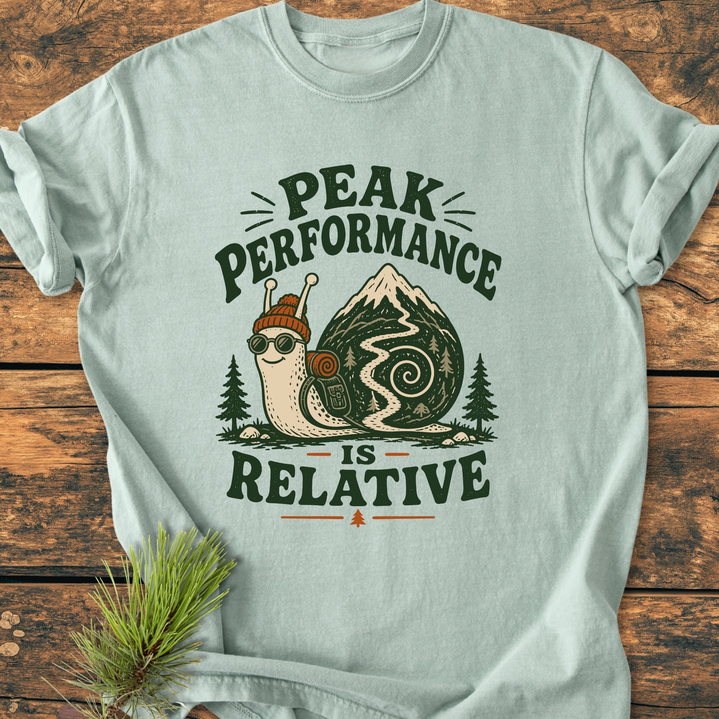 Peak Performance Is Relative - Vintage Wash Tee features a cheerful snail with a knit cap, goggles, and backpack on a mountain trail, capturing the essence of relaxed outdoor adventure.