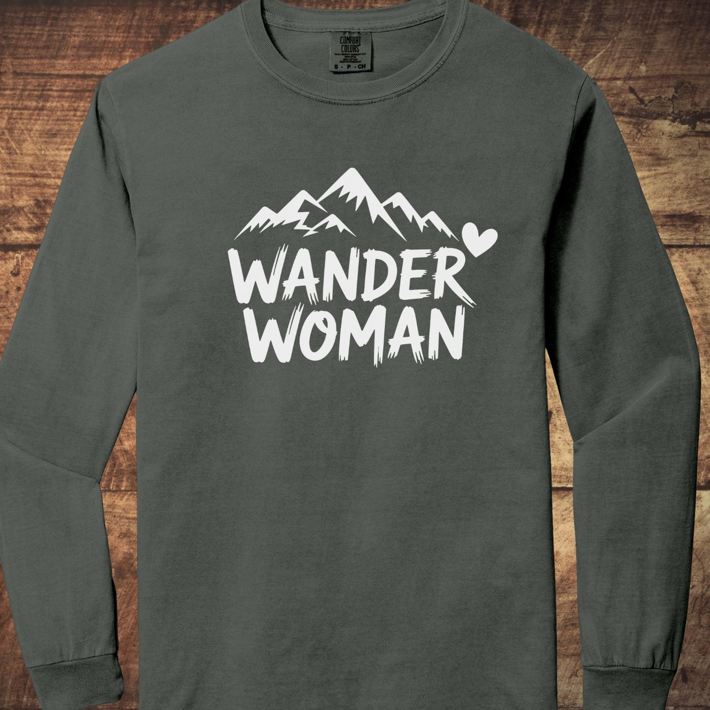 Wander Woman Comfort Colors Long-Sleeve Tee features a stylized mountain silhouette with “WANDER WOMAN” text and a heart icon, offering a relaxed fit and soft, garment-dyed 100% ring-spun cotton fabric.