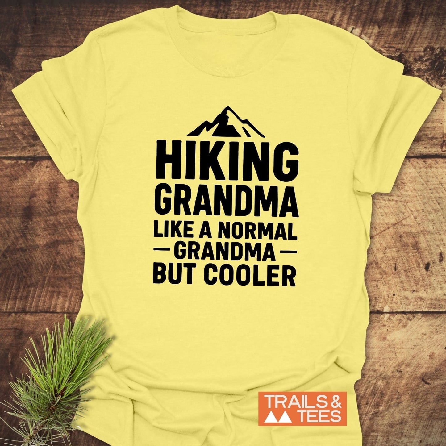Yellow T-shirt with HIKING GRANDMA and mountain graphic, showcasing Trails & Tees logo, designed for comfort and durability, perfect for outdoor-loving grandmas.