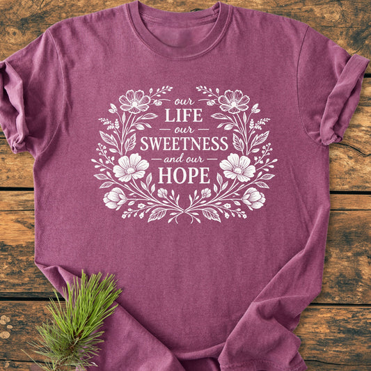 Our Life, Sweetness, Hope - Vintage Wash Tee features a hand-drawn floral wreath design on a heather-purple backdrop, laid flat with a pine sprig accentuating its woodland charm.