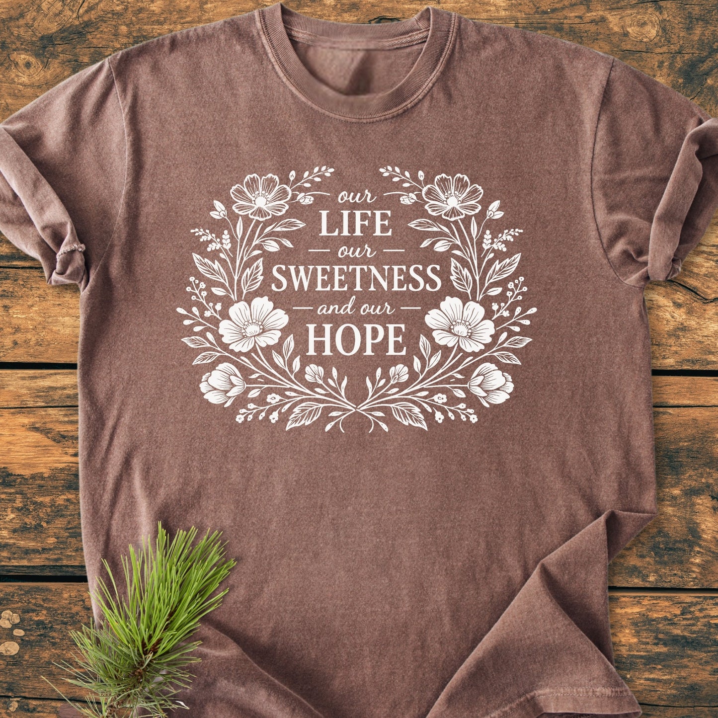 Our Life, Sweetness, Hope - Vintage Wash Tee: A brown heathered T-shirt with a floral wreath and text on chest, laid flat; pine sprig at corner, showcasing comfort and durability.
