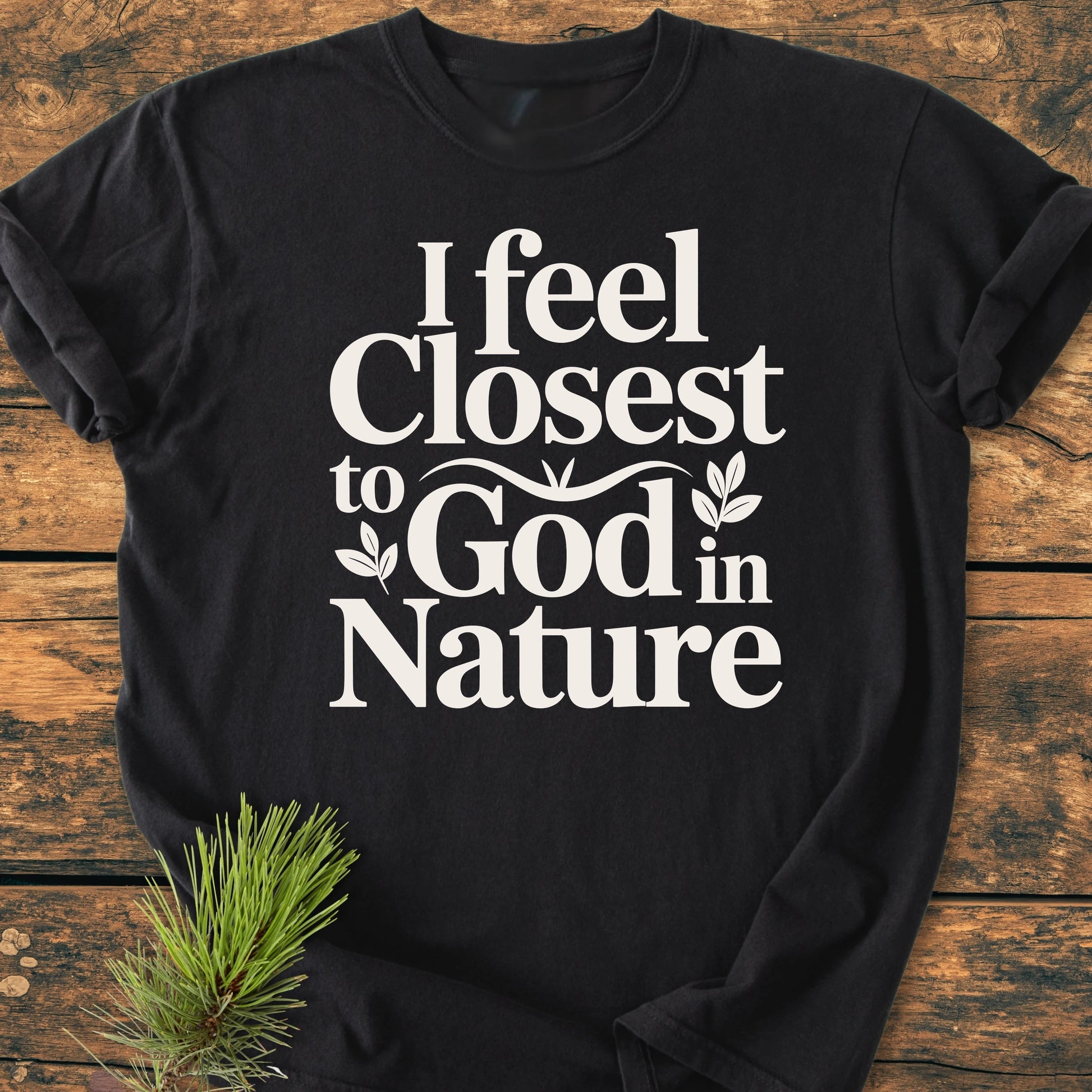 1427 Closest To God - Vintage Wash Tee featuring a relaxed unisex fit, “I feel closest to God in Nature” print with leaf accents, displayed on a wooden surface with a pine sprig.