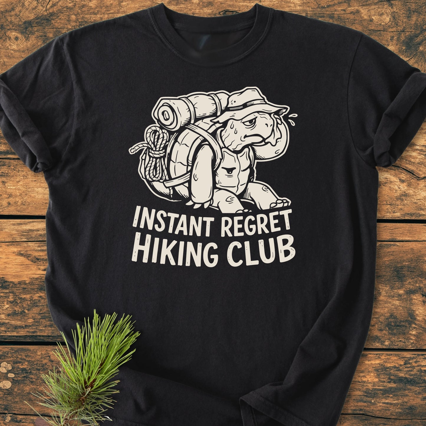 Black long-sleeved T-shirt with Instant Regret Hiking Club turtle graphic, showcasing a vintage wash and relaxed unisex fit, laid on wood, accompanied by a pine branch.