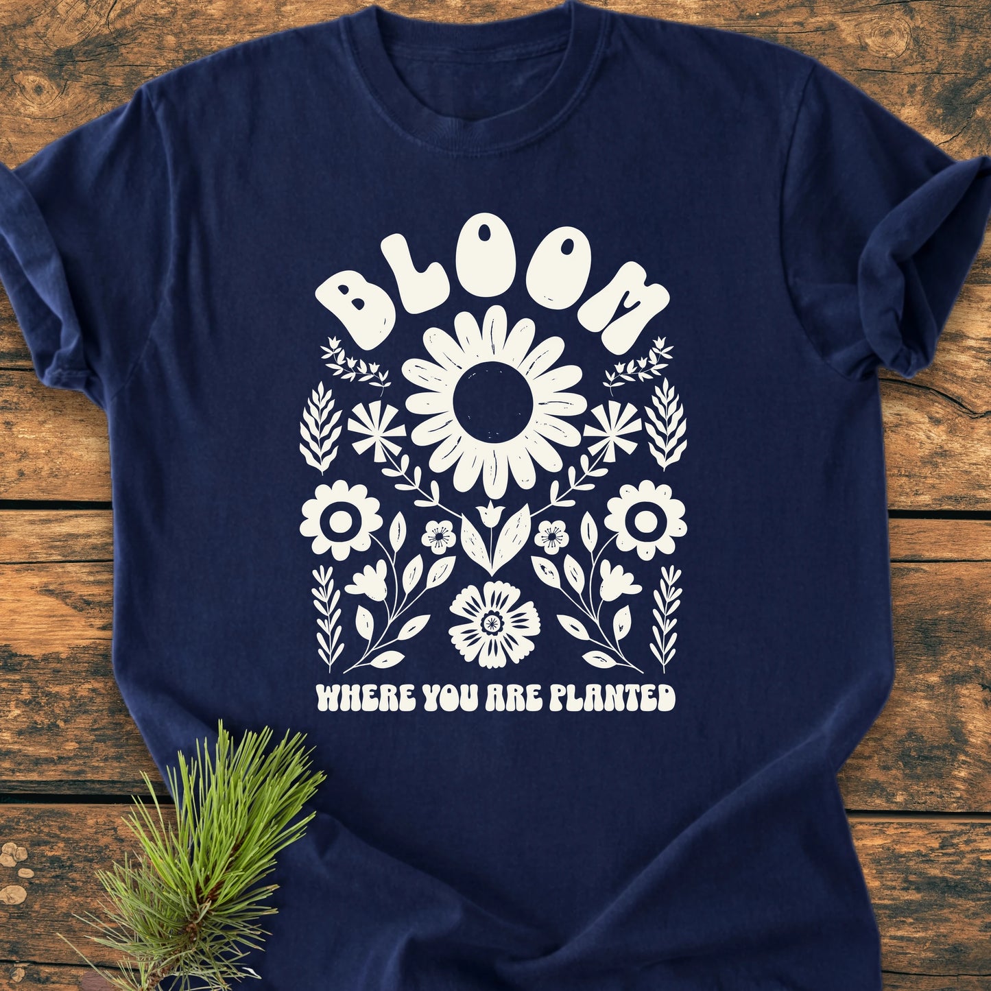 Navy-blue T-shirt featuring a stylized floral design and BLOOM WHERE YOU ARE PLANTED slogan, showcasing the 1415 Bloom Where You Are Planted's vintage, relaxed fit on a wooden surface.