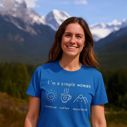 A woman smiles wearing the I'm A Simple Woman - Sunshine Coffee Mountains T-Shirt, emphasizing her relaxed style against a mountain backdrop.