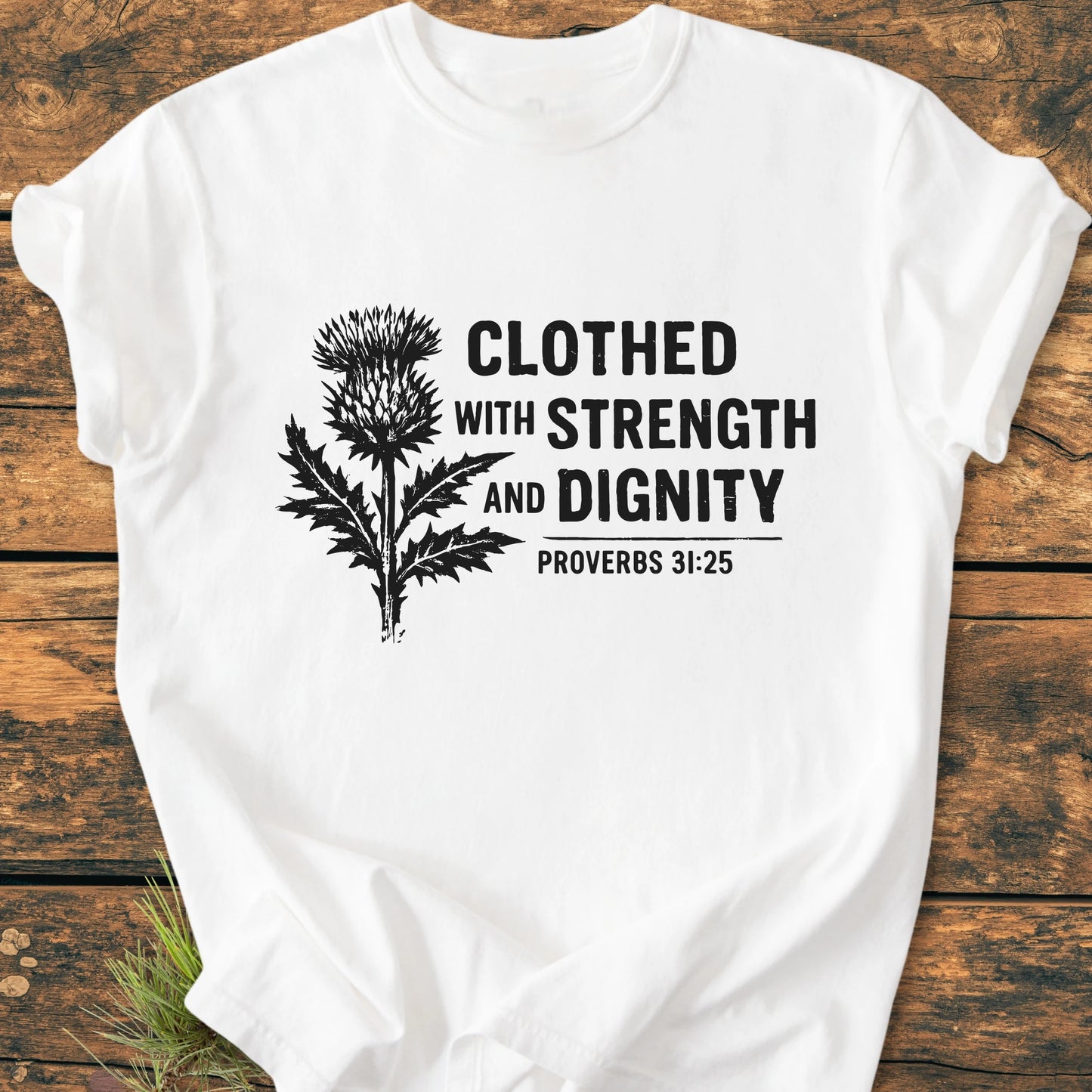 Clothed With Strength And Dignity - Vintage Wash Tee features a black thistle graphic and inspirational Proverbs 31:25 text on a soft, relaxed-fit white T-shirt, perfect for everyday comfort.