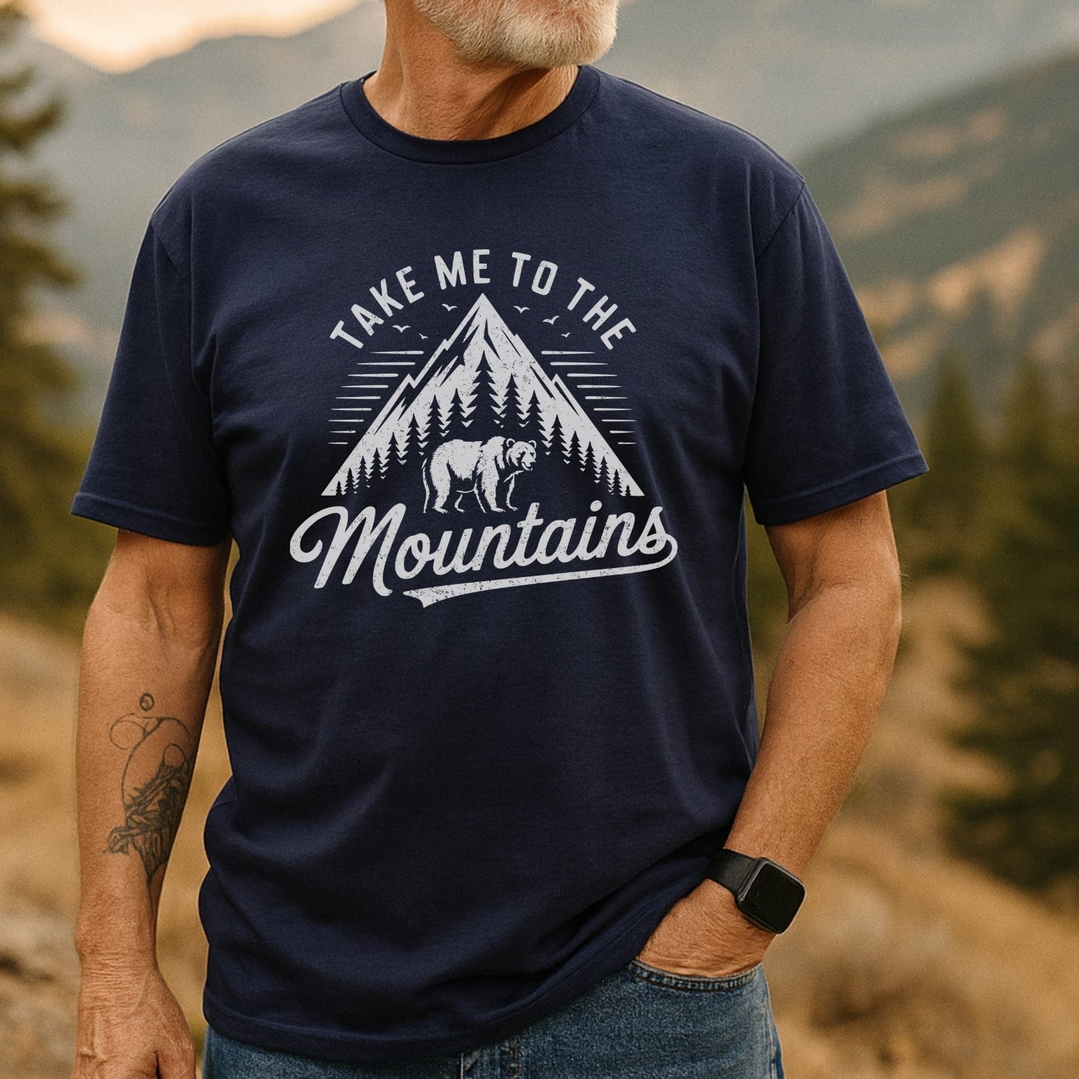 Man wearing Take Me To The Mountains T-shirt with mountain, pine-tree graphic. Soft, lightweight, perfect for adventures. Unisex fit, durable print.