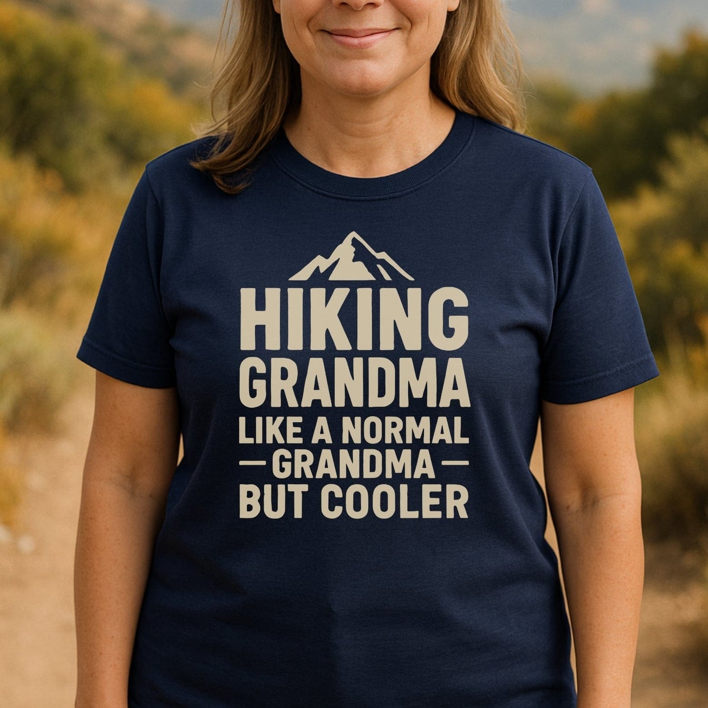 Woman wearing Hiking Grandma T-Shirt with mountain graphic, standing on a dirt path. The tee offers comfort with durable prints, ideal for outdoor enthusiasts.