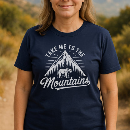 Person wearing a Take Me To The Mountains T-shirt featuring a mountain and bear design, ideal for adventures with its soft, lightweight cotton and unisex fit.