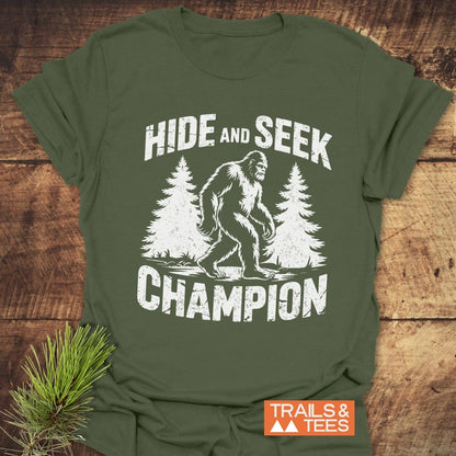 Hide And Seek Champion T-Shirt featuring a playful Bigfoot design and bold white text, perfect for active wear enthusiasts.
