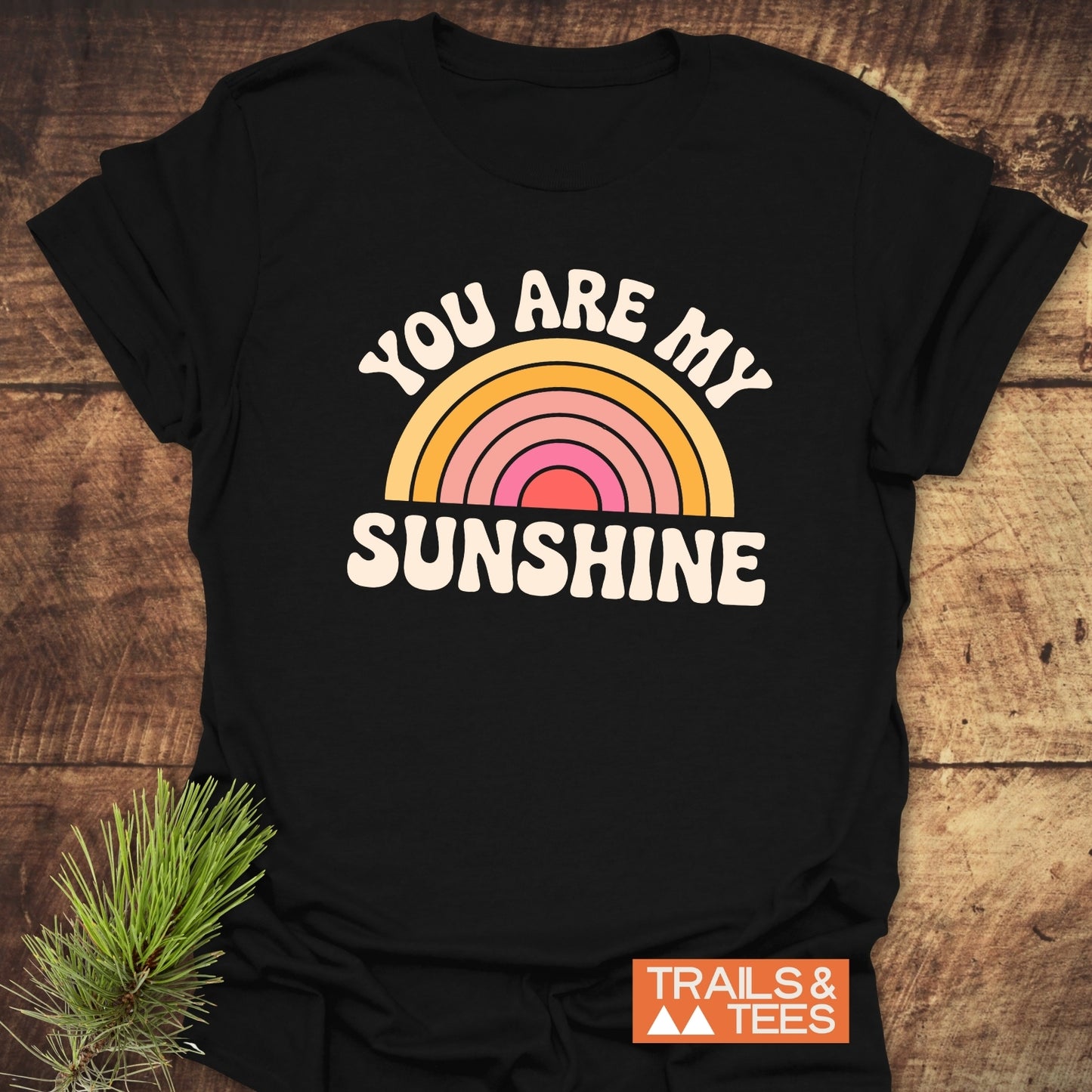 You Are My Sunshine T-Shirt featuring white text on a black shirt, complemented by a rainbow and pine branch design.