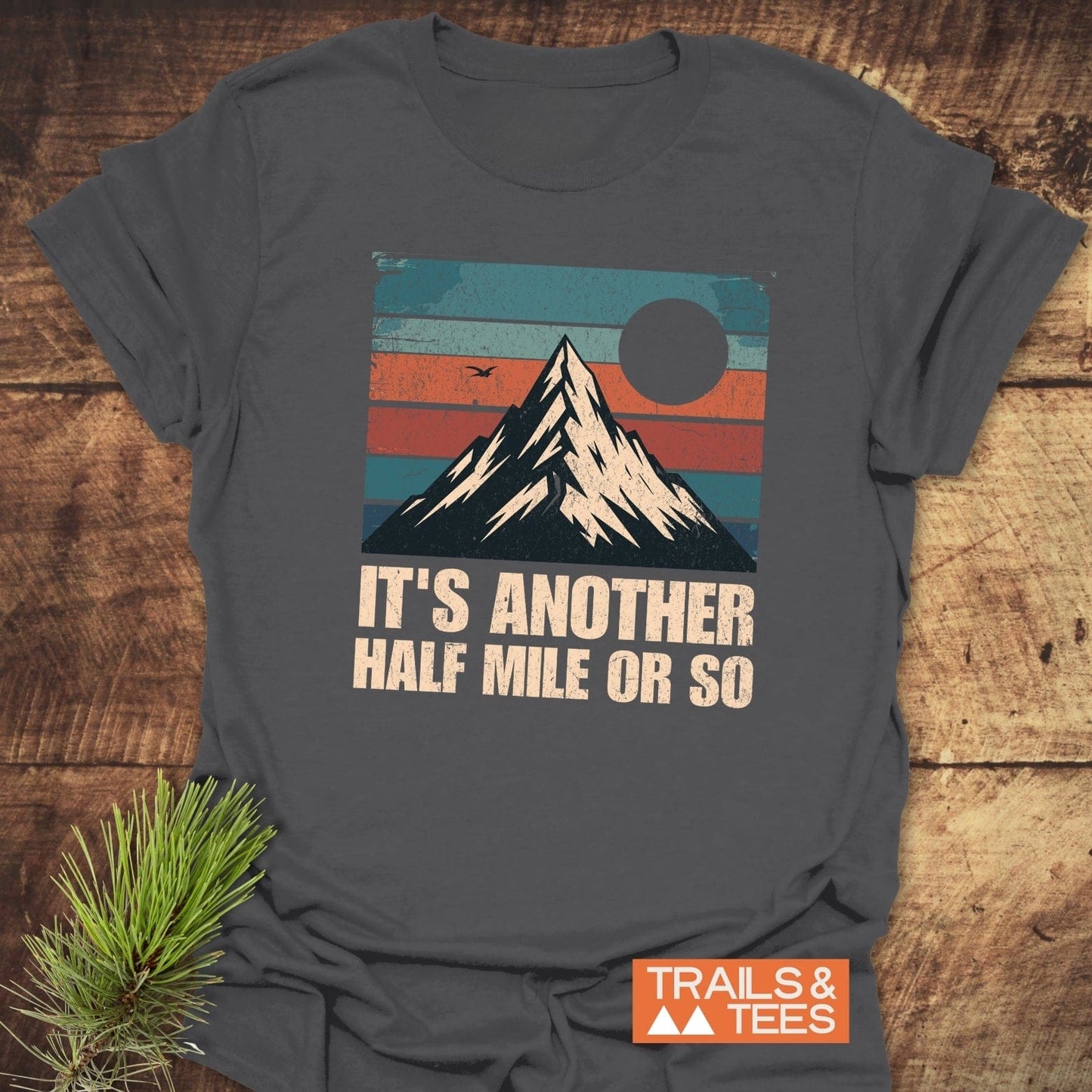 It's Another Half Mile Or So T-Shirt featuring a mountain and pine branch design, emphasizing its outdoor adventure theme.