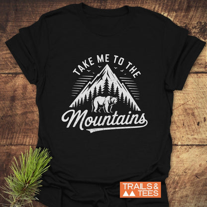Take Me To The Mountains T-Shirt showing a mountain scene with a bear, trees, and birds, emphasizing outdoor adventure with durable, comfortable design.