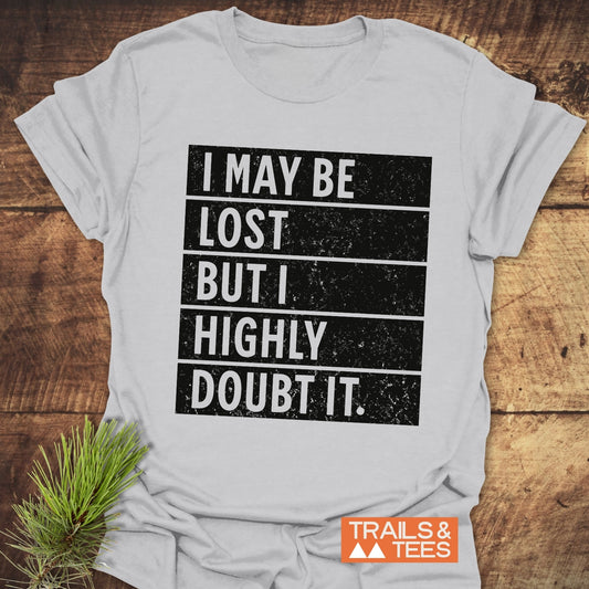 Close-up of the I May Be Lost But I Highly Doubt It T-shirt, featuring bold text, displayed alongside a black and white sign.
