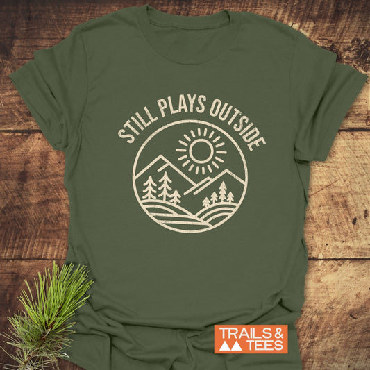 Still Plays Outside T-Shirt featuring a white graphic design on a green backdrop, crafted from soft ring-spun cotton for comfort and durability.