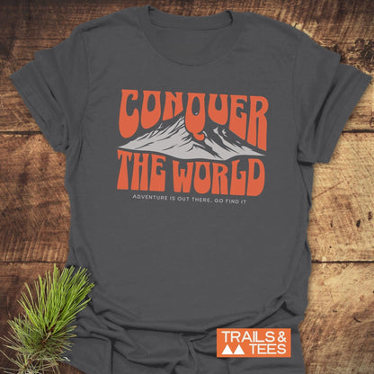 Conquer The World T-Shirt featuring bold orange text and a subtle logo, paired with a pine branch accent for an adventurous touch.