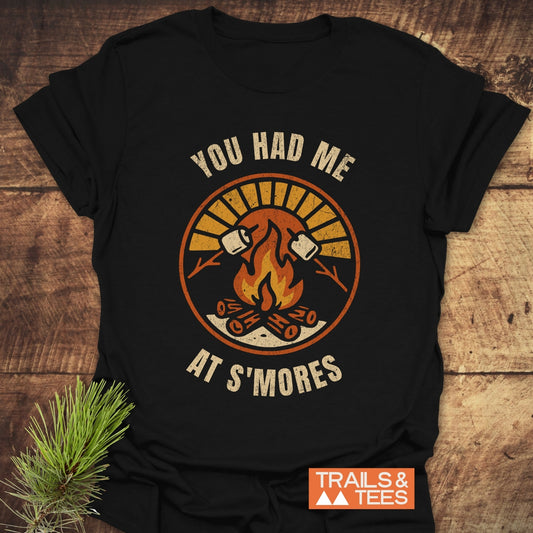 You Had Me At S'mores T-Shirt featuring a black design with white text and a drawing of a fire and marshmallows, crafted for outdoor comfort.