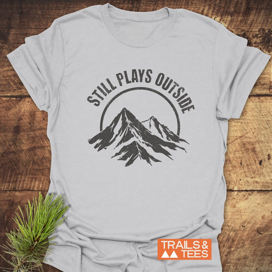 Still Plays Outside T-Shirt featuring a mountain graphic, crafted from soft ring-spun cotton, pre-shrunk for fit, and designed for outdoor enthusiasts.