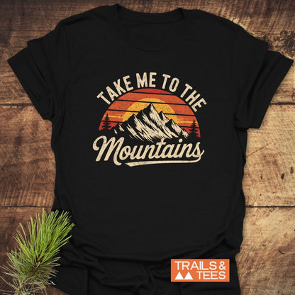 Take Me To The Mountains T-Shirt featuring a mountain and pine branch graphic design, ideal for those who love outdoor adventures.