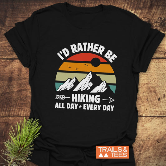 I'd Rather Be Hiking All Day Every Day T-Shirt with bold white text on a black shirt, displayed flat on a table.