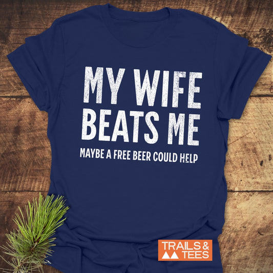 Navy-blue T-shirt with distressed white text: MY WIFE BEATS ME MAYBE A FREE BEER COULD HELP, featuring a small TRAILS & TEES logo.