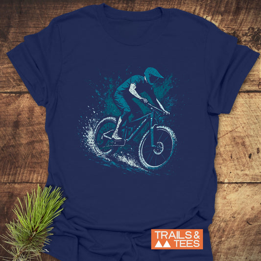 Dynamic Mountainbiker T-Shirt featuring a helmeted rider illustration, laid on a wooden surface with TRAILS & TEES logo and evergreen sprig for outdoor flair.