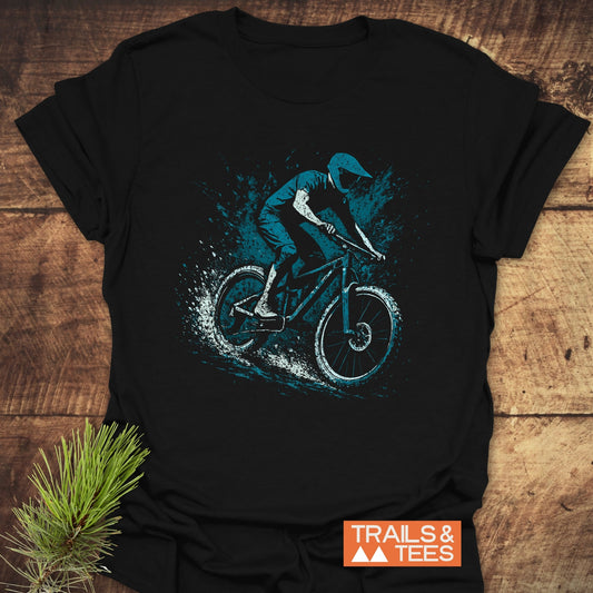Dynamic Mountainbiker T-Shirt featuring a mountain biker graphic, crafted from soft cotton for comfort and durability, laid on a wooden surface with pine sprig.