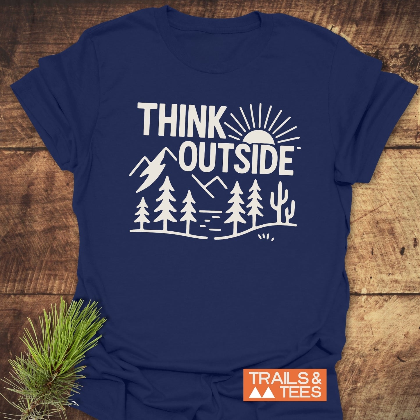 Think Outside Hiking T-Shirt featuring a white outdoor scene print on navy-blue fabric, laid on wood, highlighting its adventure-ready design and comfort.
