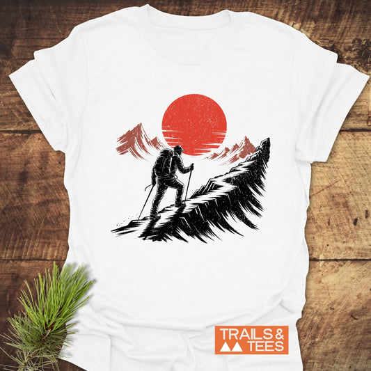 Hiker Sunset T-Shirt featuring a hiker on a jagged ridge with a red sun and mountain silhouettes, crafted from soft cotton for outdoor enthusiasts.