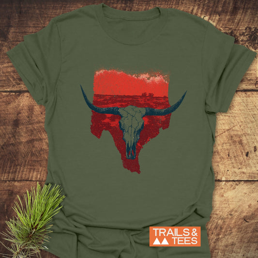 Hike Texas T-Shirt: Olive-green tee with Texas silhouette and longhorn skull design, laid on wood. Soft, durable cotton ideal for outdoor adventures.