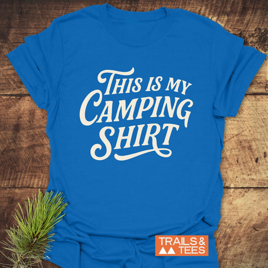 This Is My Camping T-Shirt flat-lay on wood, featuring durable white lettering, built for comfort and outdoor adventures, with Trails & Tees logo.