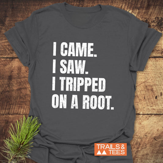 Dark-grey I Came. I Saw. I Tripped... T-Shirt with white text, laid on wood. Features Trails & Tees logo and pine branch.
