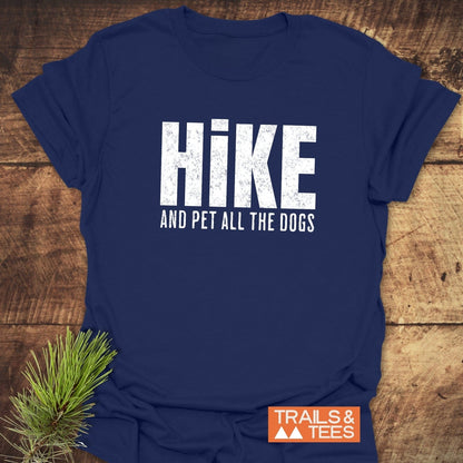 Hike And Pet Dogs T-Shirt on a wooden surface, featuring distressed white lettering. Includes a small pine sprig and “TRAILS & TEES” logo.