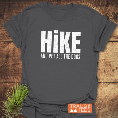 Hike And Pet Dogs T-Shirt with distressed white lettering, featuring a small orange TRAILS & TEES logo, styled with a pine branch beside it.