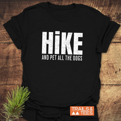Black Hike And Pet Dogs T-shirt on wood, with pine sprig, featuring distressed white slogan. Logo TRAILS & TEES visible, showcasing outdoor adventure spirit.