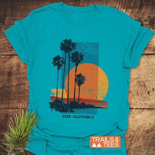 Hike California T-Shirt with retro sunset, palm trees, and coastline design. Trail-tested comfort, soft cotton, durable print, featuring Trails & Tees logo.