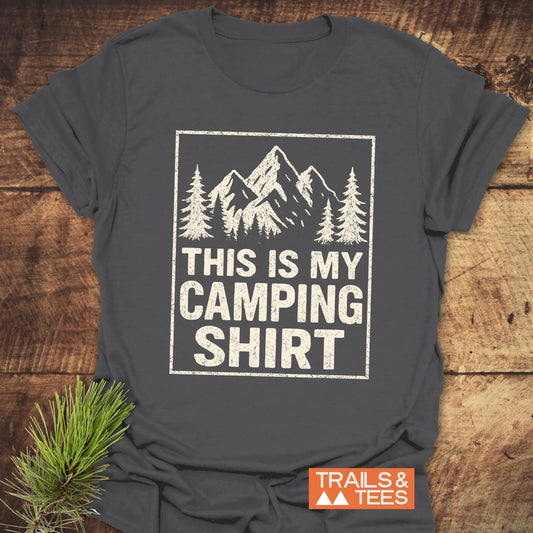 This Is My CAMPING T-Shirt featuring mountain graphic and text, laid flat with TRAILS & TEES label; soft, durable ring-spun cotton, perfect for outdoor enthusiasts.