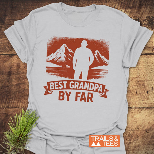 Best Grandpa By Far T-Shirt featuring a mountain silhouette graphic, laid flat with a pine sprig beside it, showcasing Trail-tested comfort and durable design.