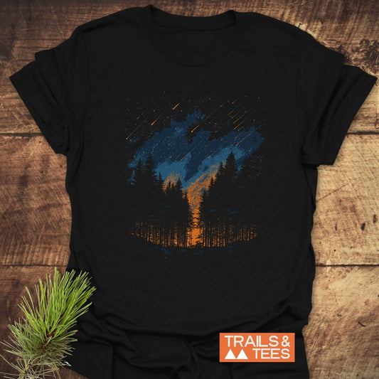 Sunset Forest T-Shirt featuring a stylized forest scene with pine trees, orange horizon, and shooting stars, laid flat with Trails & Tees logo visible.