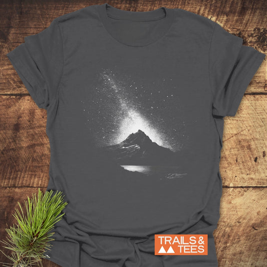 Starry Sky Above T-Shirt laid flat, showcasing a mountain graphic under a starry sky. Made from soft cotton, ideal for outdoor enthusiasts.
