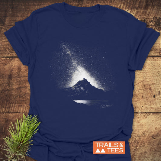 Navy-blue Starry Sky Above T-Shirt with a mountain and starry sky graphic, featuring orange TRAILS & TEES logo, on rustic wood surface.