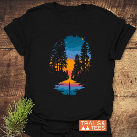 Into The Light T-Shirt featuring a mirrored forest sunset design, laid flat with a pine sprig, showcasing its trail-tested comfort and durable print.
