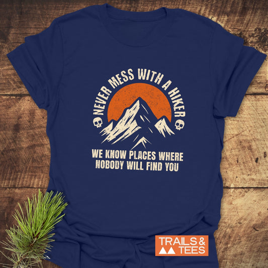 Never Mess With A Hiker T-Shirt featuring a mountain graphic with sun, bold text, and skull icons. Made from soft cotton, durable, and pre-shrunk.