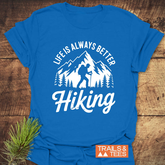 Life Is Always Better Hiking T-Shirt with mountain, trees, and hiker design. Soft, durable cotton with pre-shrunk fit, promoting outdoor adventure. Includes TRAILS & TEES logo.