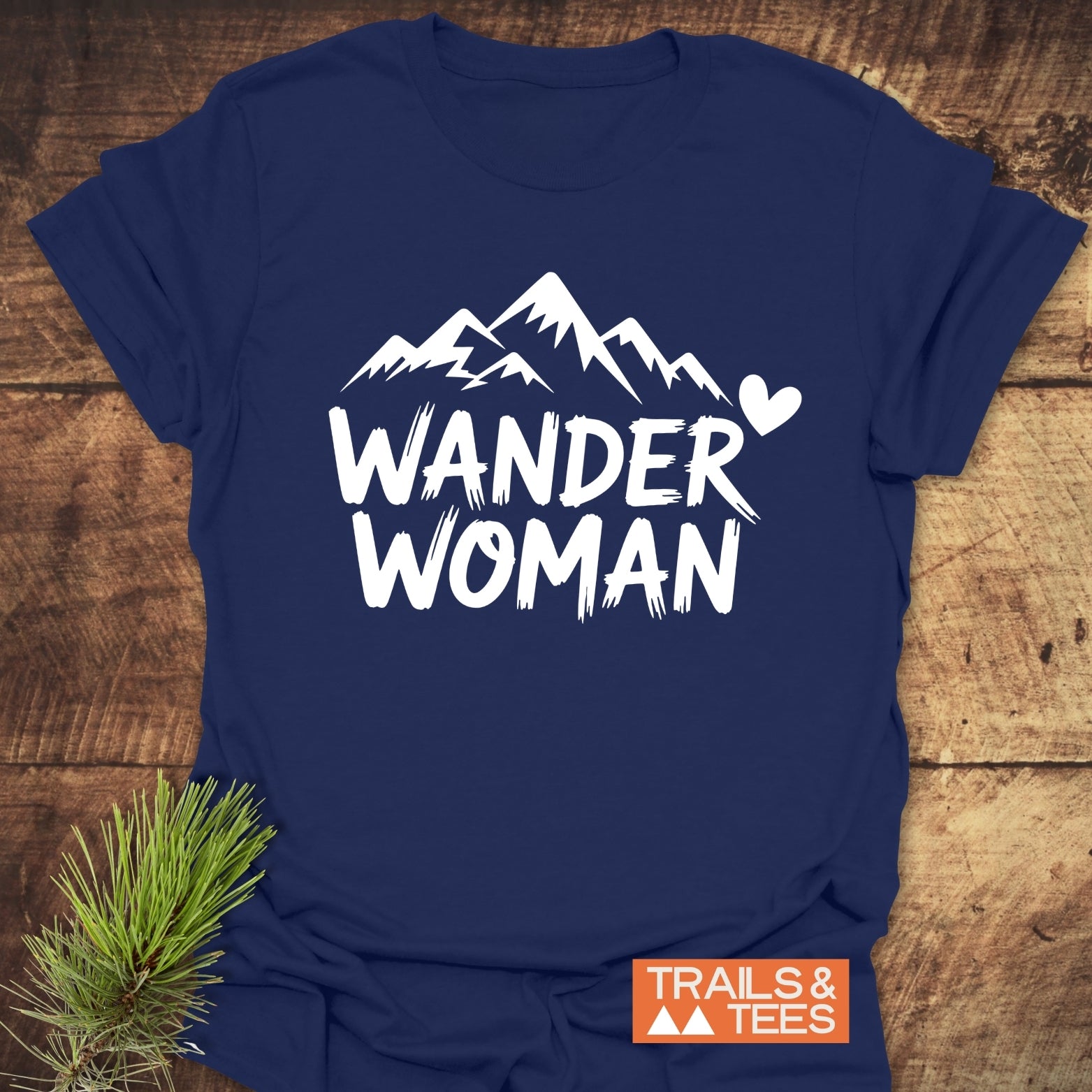 Wander Woman T-Shirt with mountain silhouette and heart, displayed on wood. Made from soft ring-spun cotton, pre-shrunk, featuring durable prints for outdoor enthusiasts.