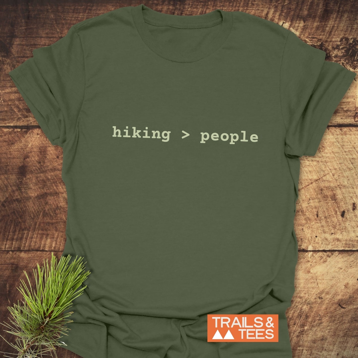 Olive-green Hiking > People T-shirt on wood, featuring typewriter font. Trails & Tees logo visible, highlighting outdoor adventure and comfort.